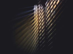 Dramatic light and shadows cast through window blinds, creating a moody atmosphere.