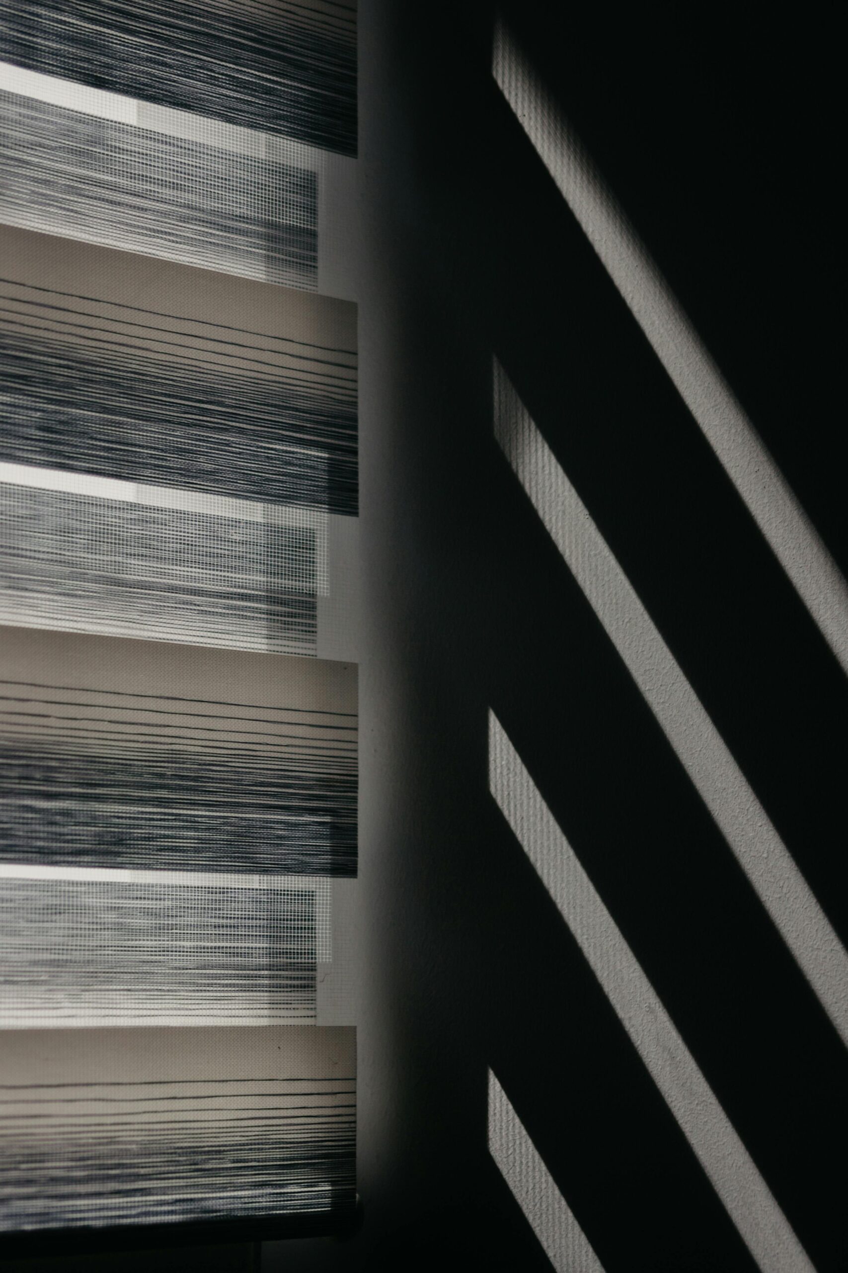 Modern window blinds create striking shadows on a wall for an abstract visual effect.